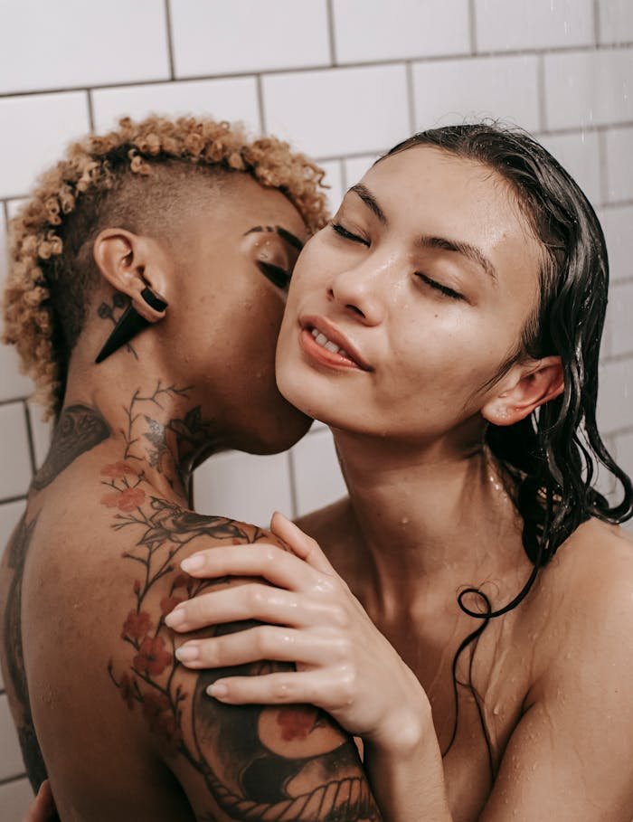 Side view of sensual undressed multiethnic same sex couple kissing and hugging gently while standing in shower